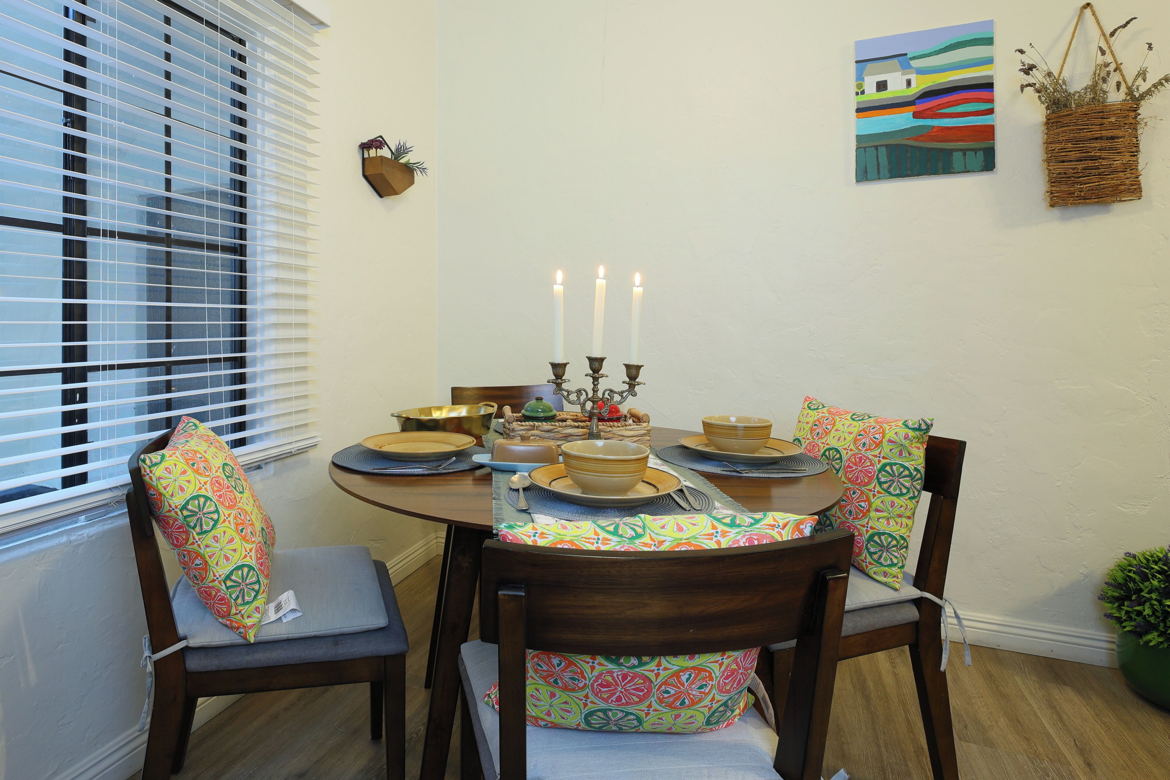 A dining table set with plates, bowls, and candles. There are chairs with patterned cushions.