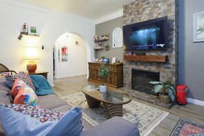 A cozy living room with a fireplace, a flat-screen TV mounted above it, a comfortable sofa with colorful cushions, and a coffee table.