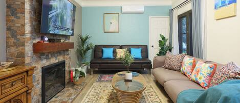 Una sala de estar con chimenea, televisor de pantalla plana, sofá con cojines de colores y una mesa de centro.