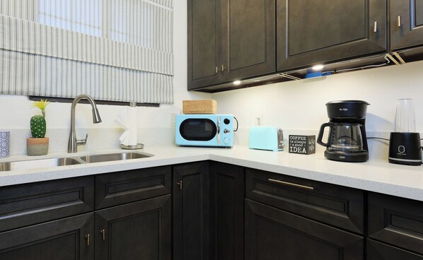A modern kitchen with dark cabinets, a stainless steel sink, a blue microwave, a coffee maker, and a toaster.
