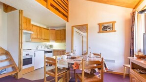 A dining area with a wooden table and chairs, a kitchen with wooden cabinets, and a window with curtains. - 100m from ski slopes, 3rd floor, view mountain, balcony, tv, ski locker, 45m², Montchavin La Plagne (Bellentre)