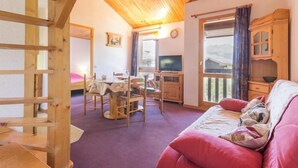 A cozy room with a wooden ceiling, a red sofa, a dining table with chairs, and a television. - 100m from ski slopes, 3rd floor, view mountain, balcony, tv, ski locker, 45m², Montchavin La Plagne (Bellentre)