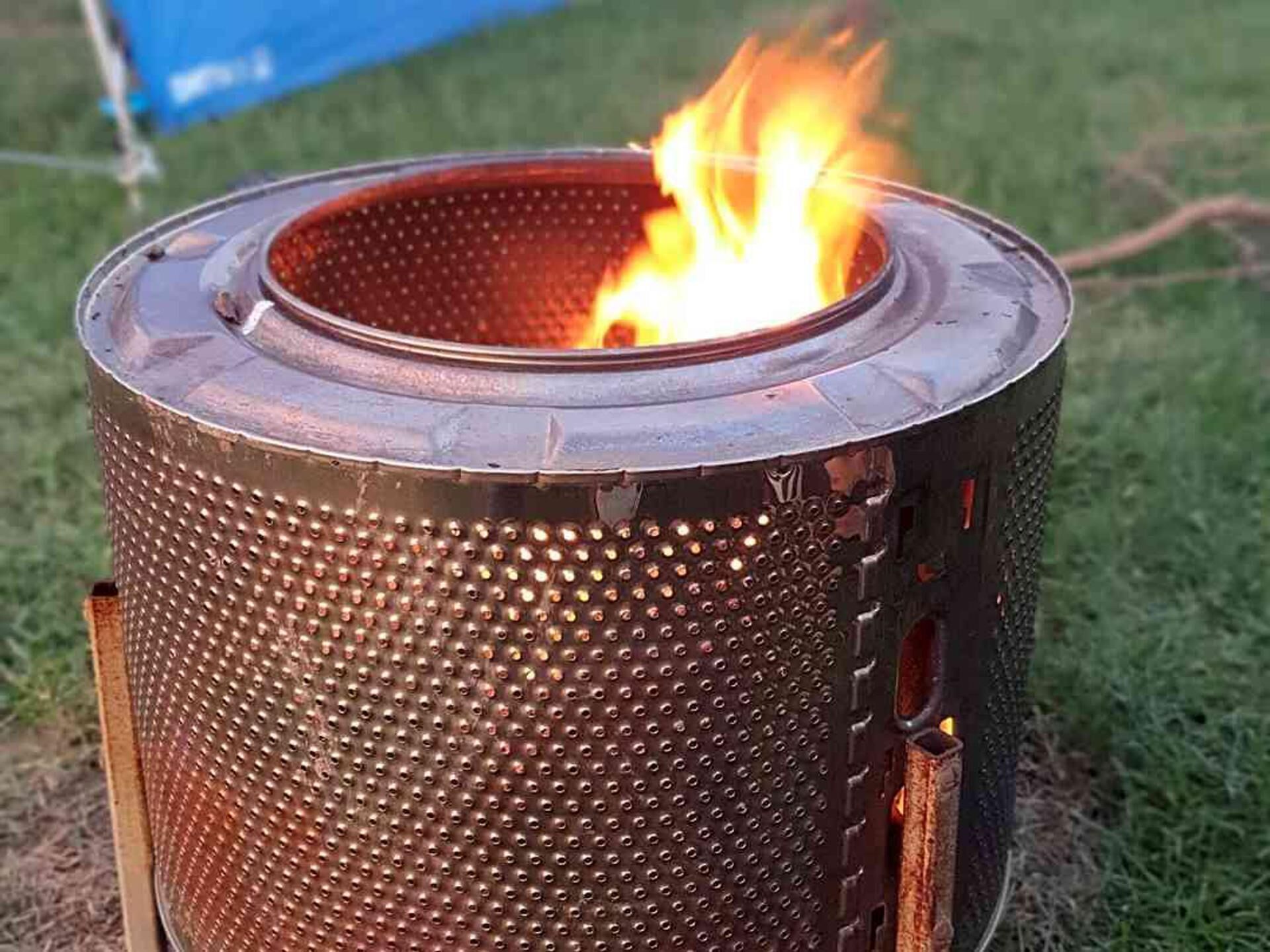 A cylindrical metal fire pit with a perforated exterior, emitting flames.