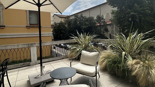 Un patio al aire libre con una mesa, sillas, un paraguas grande y plantas en macetas.