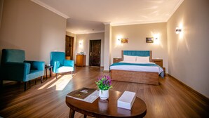 A hotel room with a wooden floor, a bed with a blue headboard, two blue armchairs, a small table with a vase of flowers, and two wall-mounted lights. - Pyramids Chill Out (Giza)