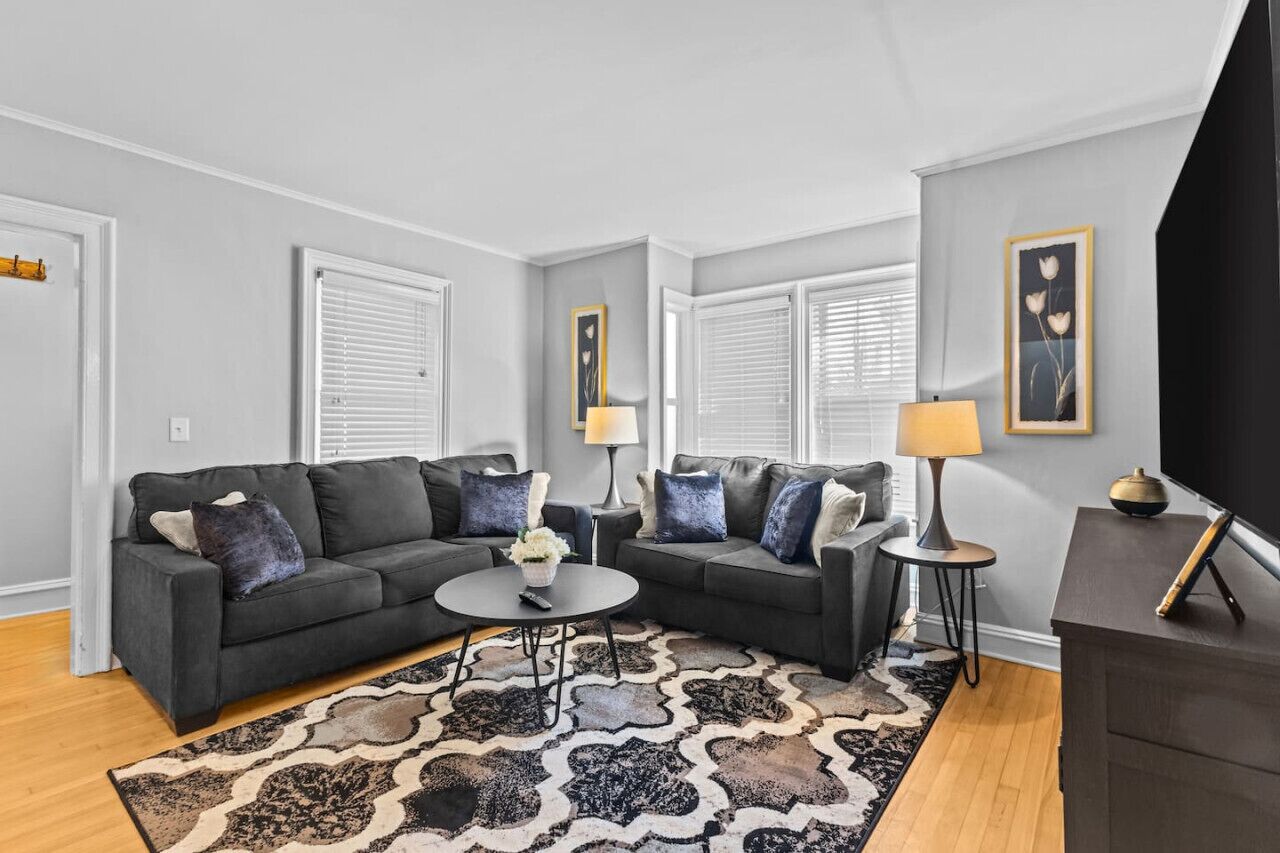 Un salon moderne avec un canapé d’angle, deux tables d’appoint, une table basse et un tapis à motifs.