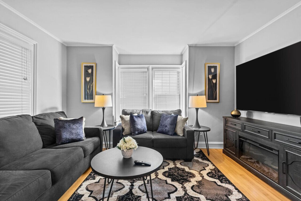 Un salon moderne avec un canapé gris, une table basse et un téléviseur. On y trouve deux lampes et une cheminée.