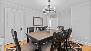 Una sala da pranzo con tavolo e sedie in legno, un lampadario e uno specchio appeso al muro.