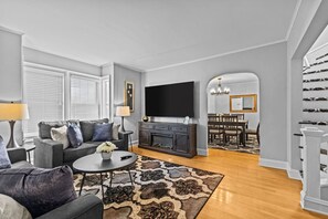 A modern living room with a grey sofa, a coffee table, and a flat-screen TV. - Charming 4BR House - Burlington (Burlington)