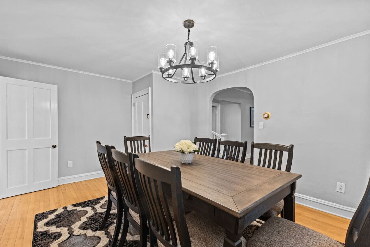 A dining room with a wooden table, six chairs, a chandelier, and a rug.