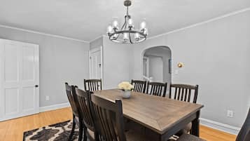 A dining room with a wooden table, six chairs, a chandelier, and a rug.