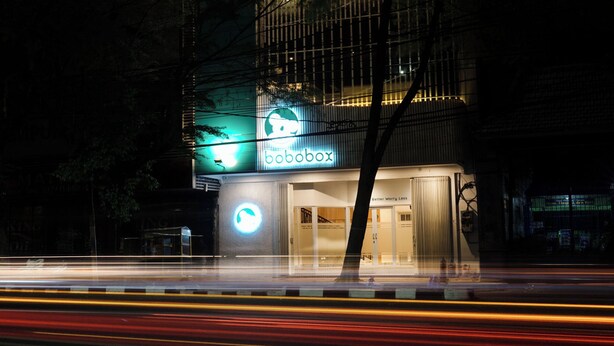 Un edificio con un letrero que dice 'bobobox', una entrada visible y un letrero circular iluminado en el suelo.