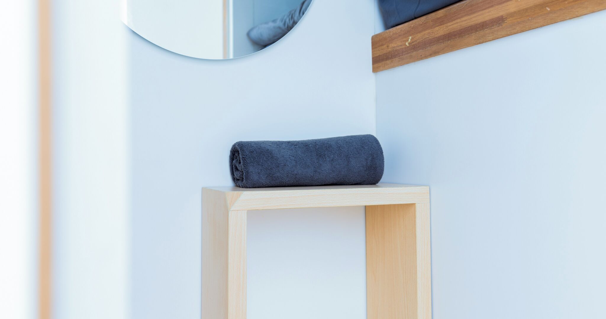 A wooden stool with a dark blue towel placed on top, positioned against a light-colored wall.