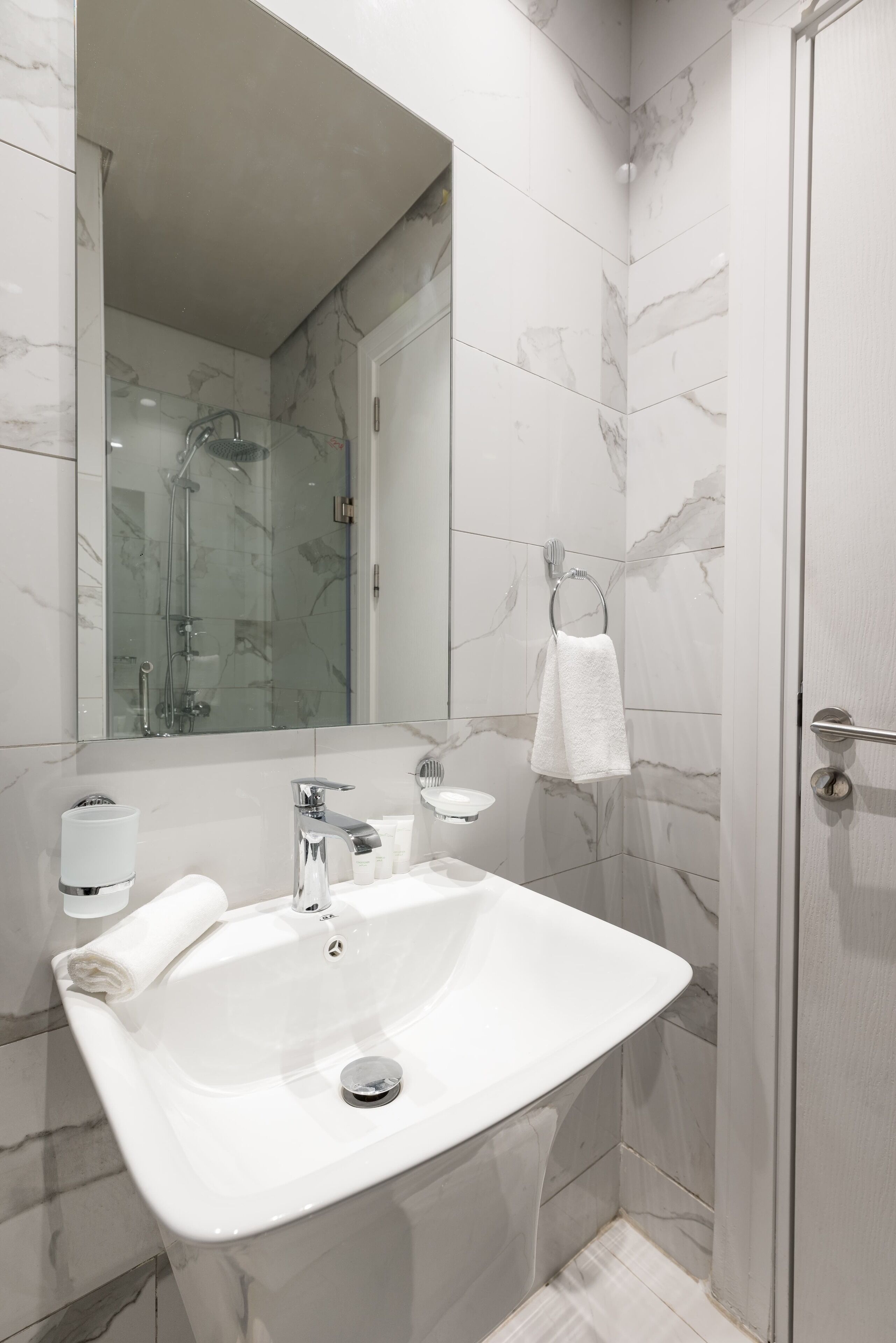A modern bathroom with a marble-tiled shower, a white sink, and a glass-enclosed shower area.