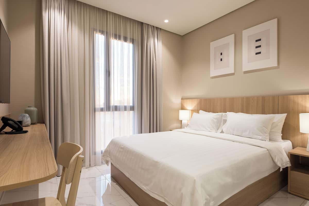 A hotel room with a bed, bedside table, lamp, chair, desk, and curtains.