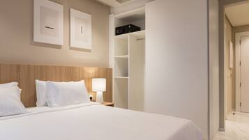 Habitación de hotel con una cama grande, cabecera de madera, armario blanco y mesita de noche con una lámpara.
