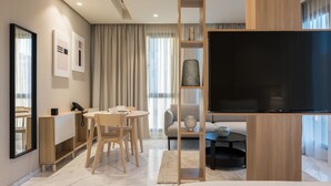 Une chambre d’hôtel moderne équipée d’un téléviseur à écran plat, d’un bureau en bois, d’une table à manger avec des chaises, d’un canapé et d’une grande fenêtre avec des rideaux.
