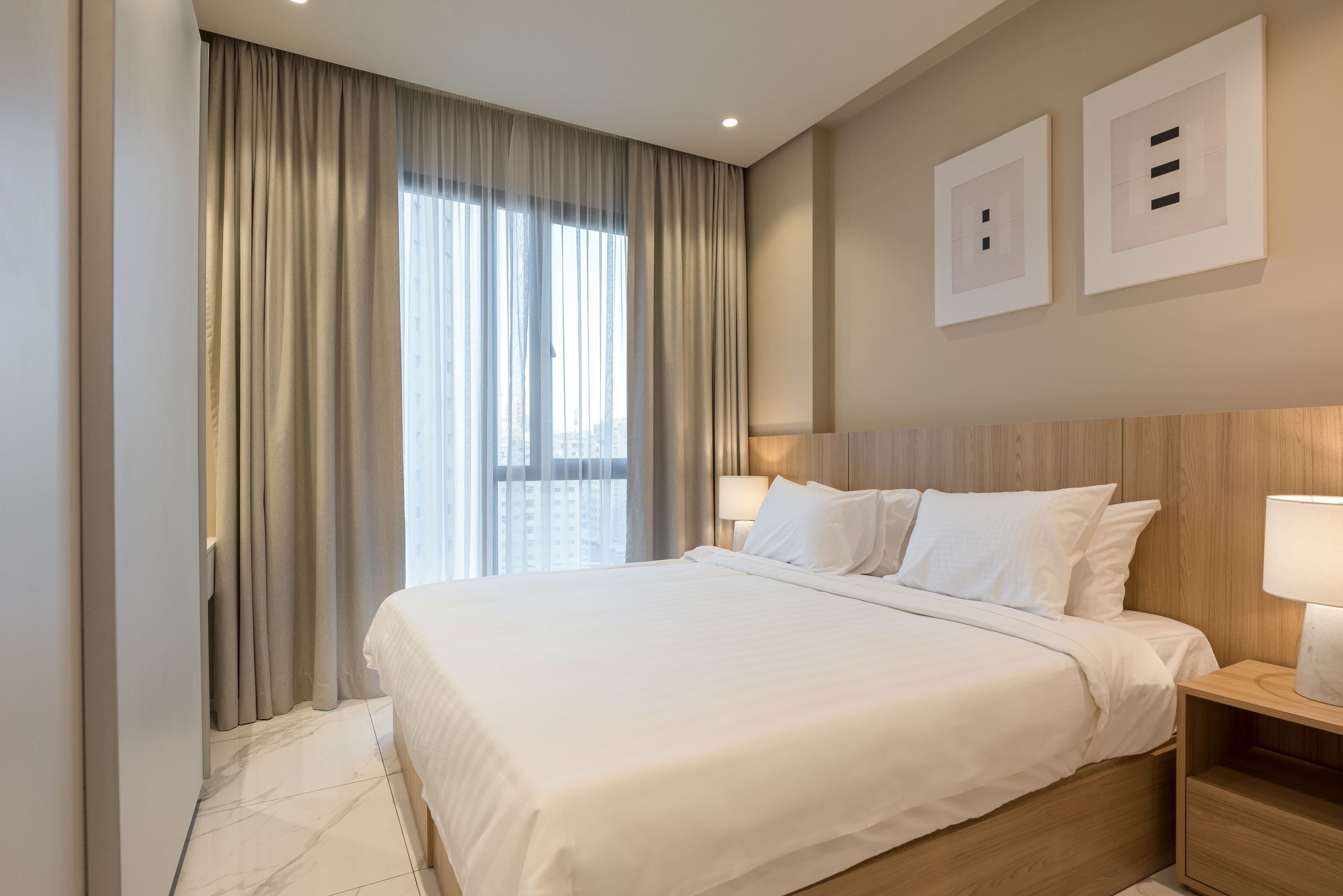 A hotel room with a large bed, a wooden headboard, a nightstand with a lamp, and a window with curtains.