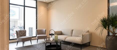 A modern living room with a sofa, chairs, a coffee table, and a large window offering a city view.