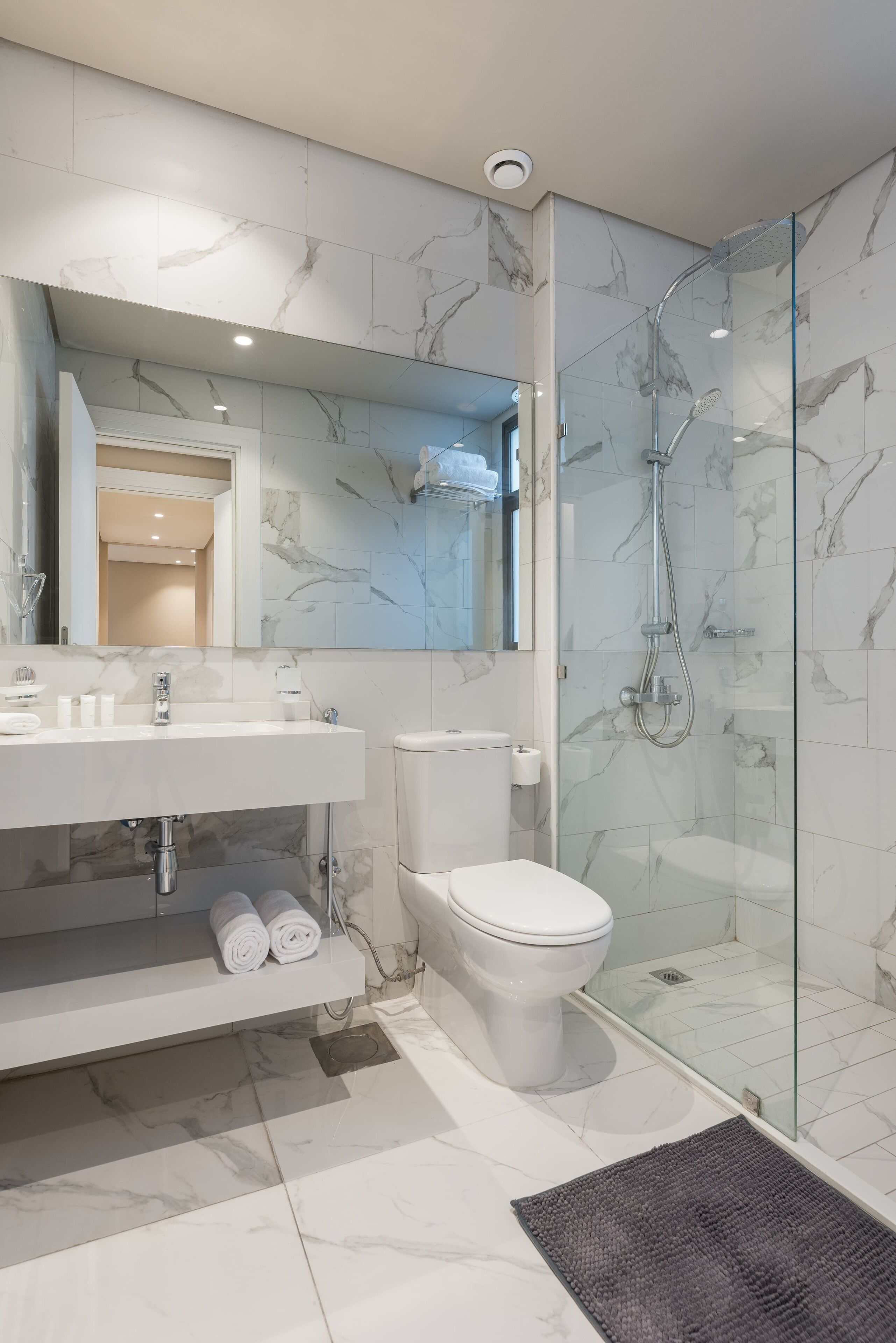 Une salle de bain moderne avec une douche à parois de verre, un lavabo blanc avec un pare-éclaboussures en marbre et des toilettes.