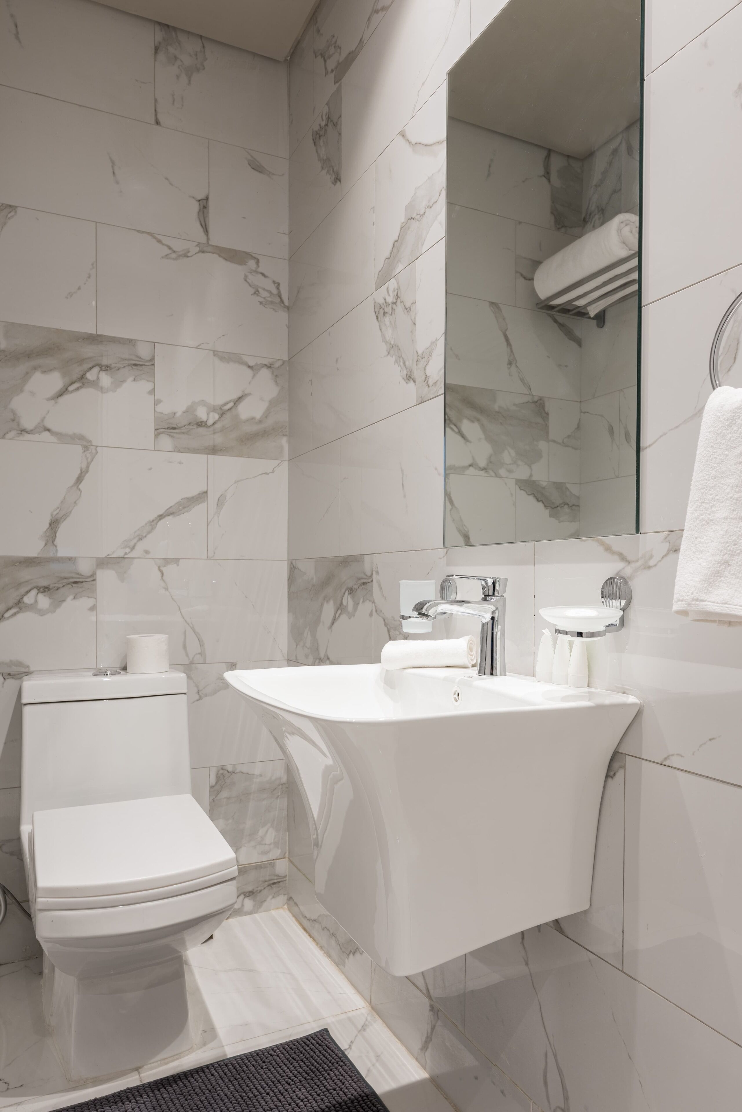 A modern bathroom with a marble backsplash, a freestanding bathtub, a toilet, and a sink with a mirror above it.