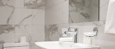 A modern bathroom with a marble backsplash, a freestanding bathtub, a toilet, and a sink with a mirror above it.