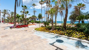 Un paseo marítimo con palmeras, parterres de flores y vista al mar.