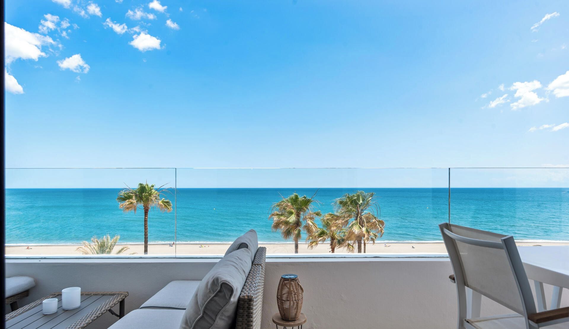 A balcony with a view of the ocean, a sofa, a chair, and a small table with candles.