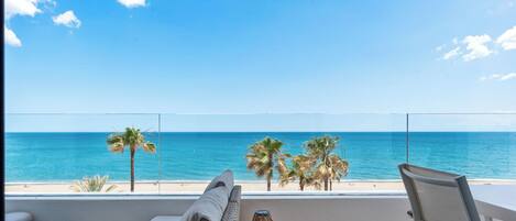 A balcony with a view of the ocean, a sofa, a chair, and a small table with candles.