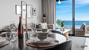 Un comedor con una mesa dispuesta para cuatro, vista al mar a través de un ventanal grande y un balcón con vistas.