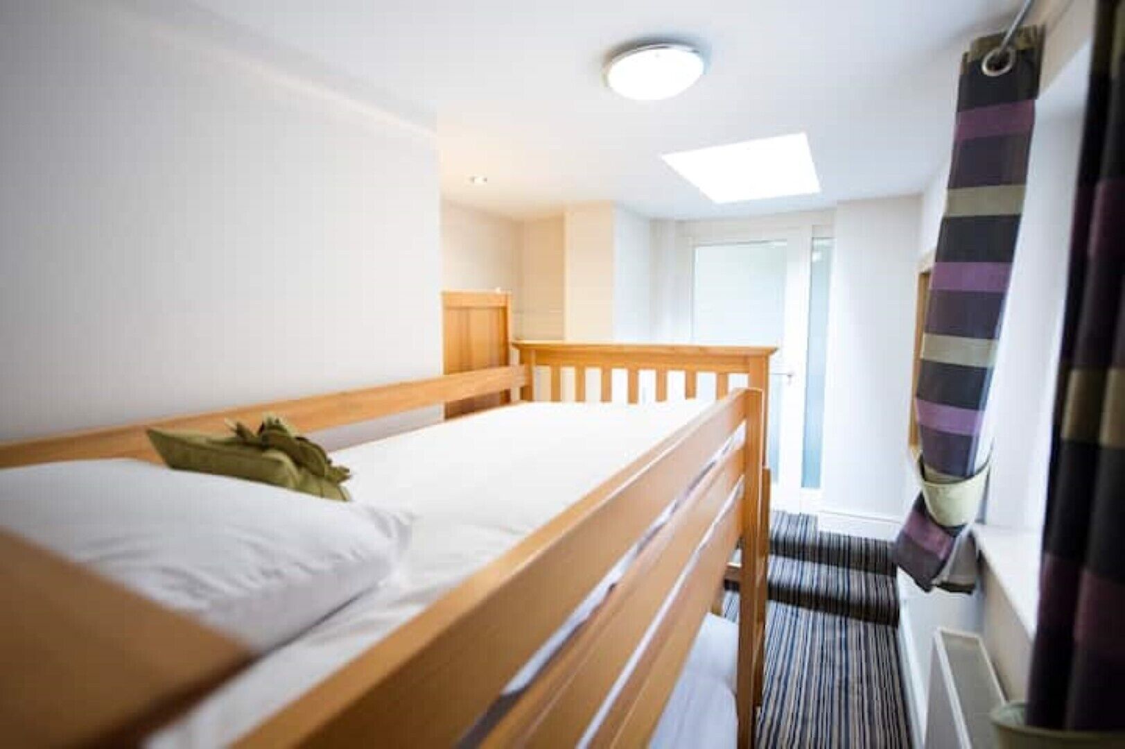 Een houten bed met wit beddengoed in een kamer met dakraam en uitzicht op het landschap.