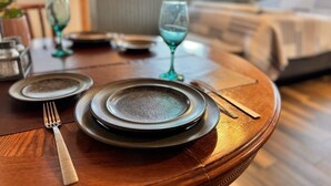 Ruokapöytä on katettu lautasilla, aterimilla ja laseilla. Huoneessa on sänky ja taustalla näkyy ikkuna.