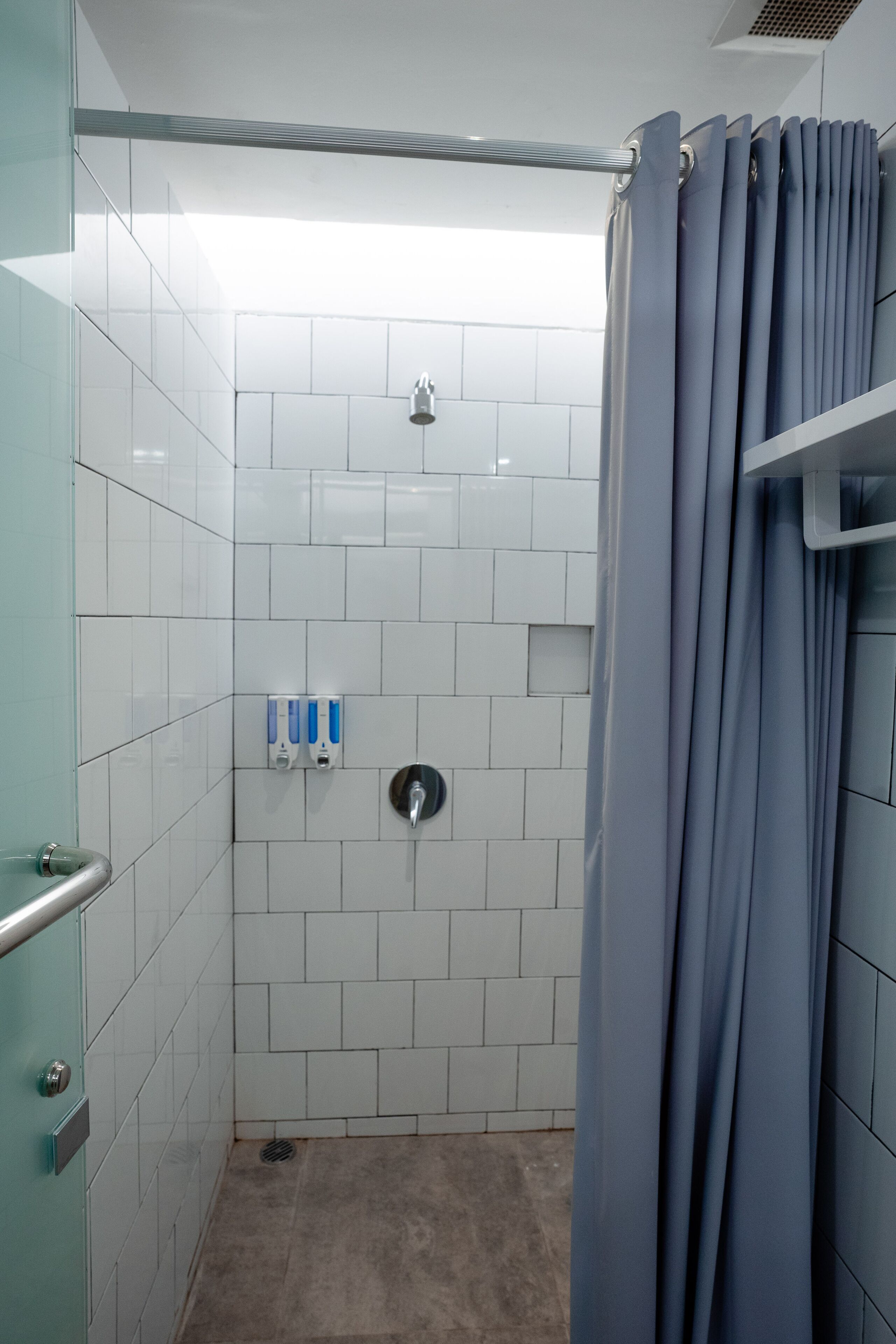 A small, tiled shower area with a glass door, a showerhead, and a hand soap dispenser.