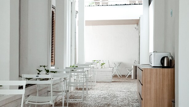 A narrow hallway with white walls, a wooden cabinet, and a small table with chairs. - Bobopod Kota Lama Semarang (Semarang)