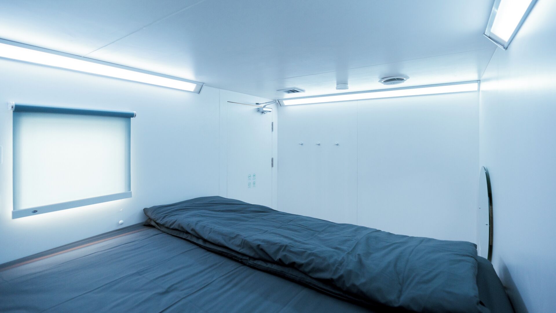 Una habitación pequeña y moderna con una cama individual, un ventanal y luces empotradas en el techo.