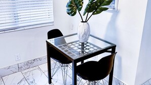 A modern dining area with a glass-top table, two black chairs, and a white vase with green leaves. - Sapphire by the Sea Unit 8 - King Pool View Suite, kitchen, pool view, Sleeps 2 (Fort Lauderdale)