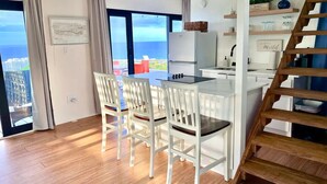 A modern kitchen with white cabinetry, a dining area with white chairs, and a view of the ocean.