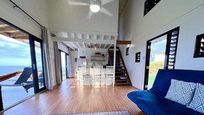 A spacious living area with a blue sofa, wooden flooring, and a view of the ocean through large windows.