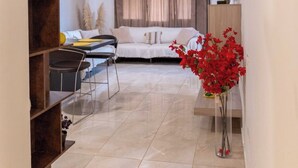 Una sala moderna con un sofá, una mesa de comedor y una mesa auxiliar. Se ve una estantería a la izquierda y un jarrón con flores rojas a la derecha.