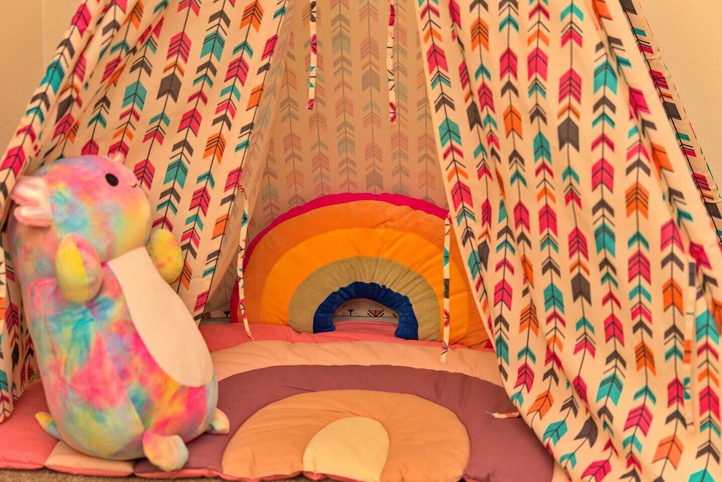 Un área de juegos con forma de carpa, con un arcoíris y un juguete de peluche grande.