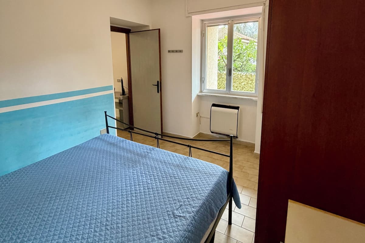 A bedroom with a bed, a window, a radiator, and a door.