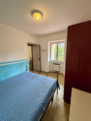 A bedroom with a bed, a window, a radiator, and a door.