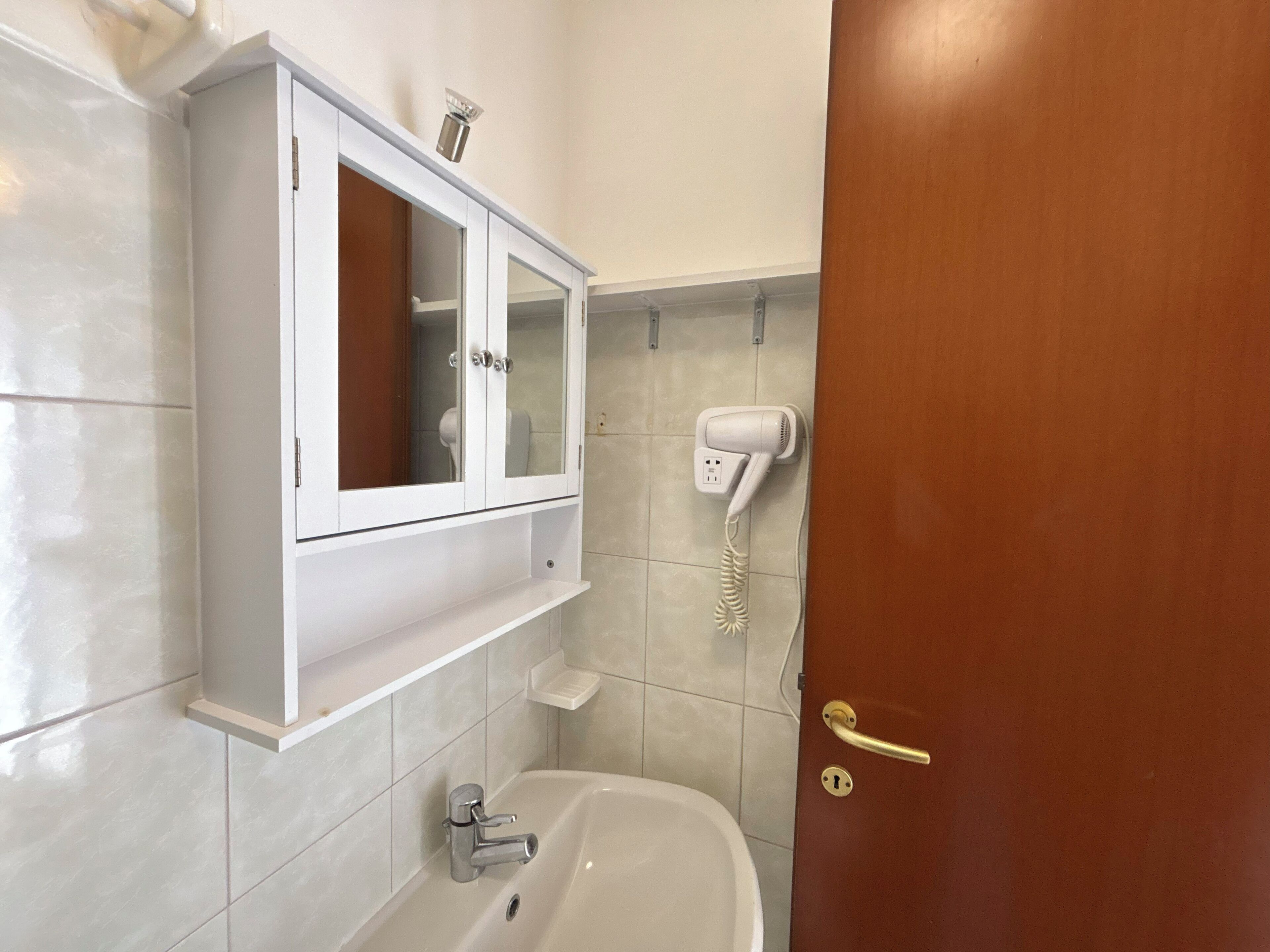 Un baño con un mueble blanco, un secador de pelo, una bañera y una puerta.