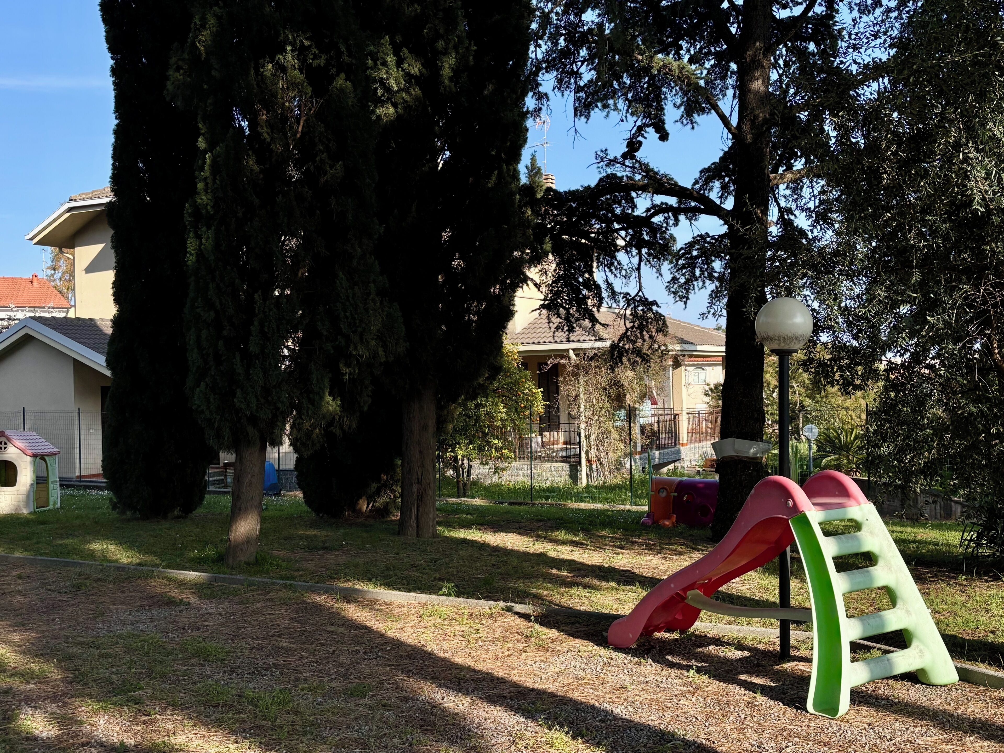 A playground with a slide and climbing structure, surrounded by trees and a building in the background.