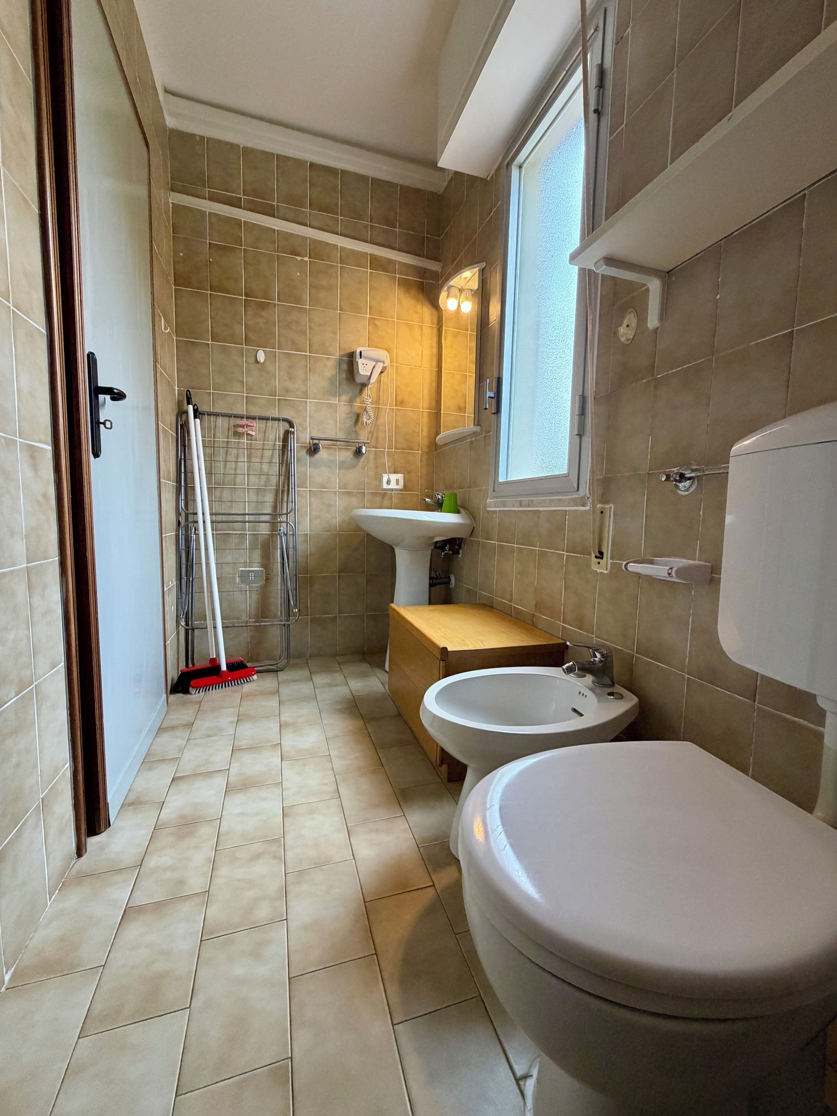A bathroom with a toilet, two sinks, a shower, and a window.