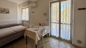 Een kamer met een bed, een tafel met tafelkleed, een stoel, een raam met gordijnen en een schuifdeur met glas.