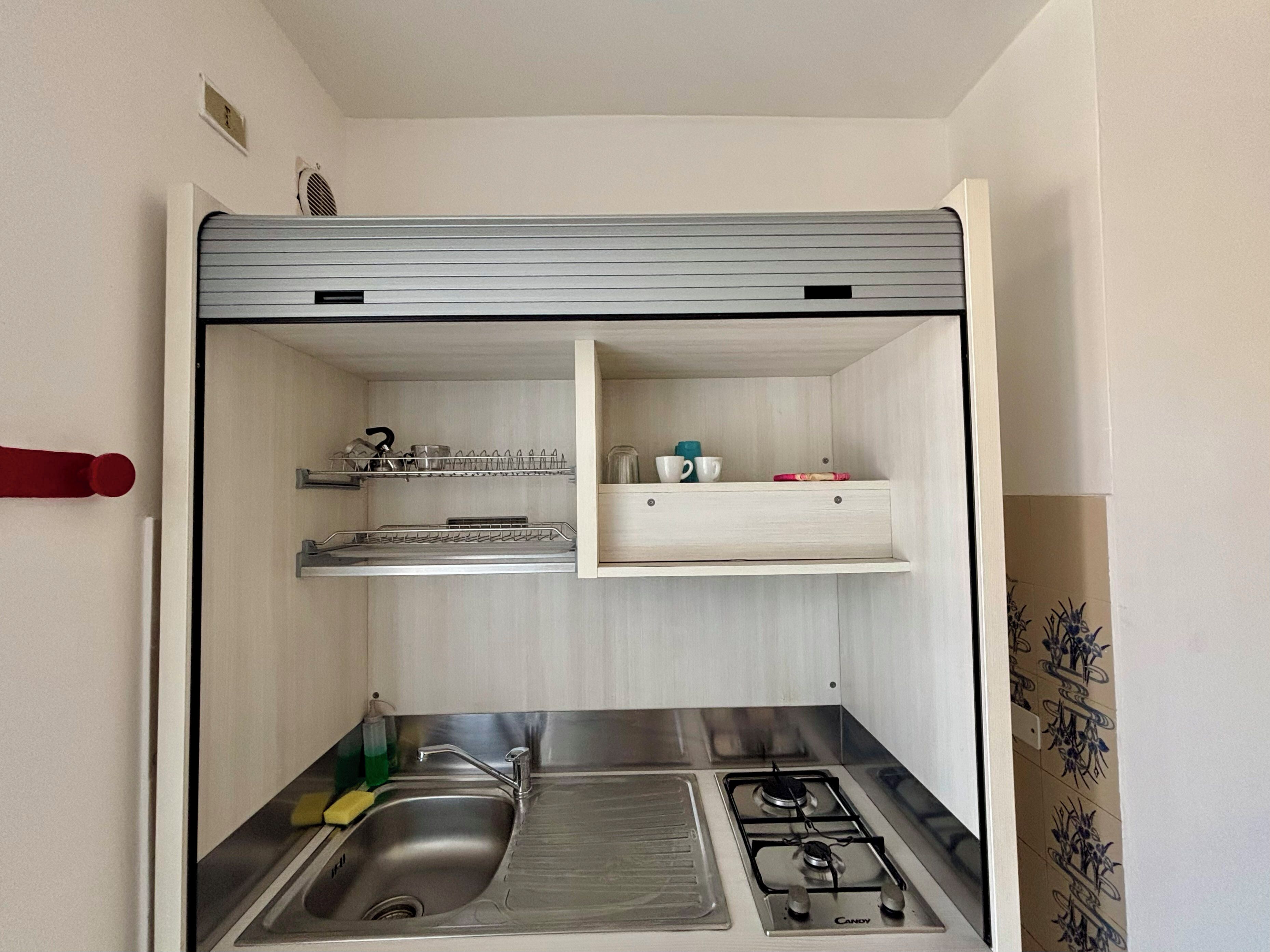 A compact kitchen with a sink, stove, and shelves for storage.
