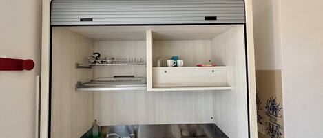 A compact kitchen with a sink, stove, and shelves for storage.