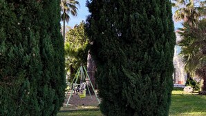 Een tuin met een schommel, een bankje en een grote naaldboom.