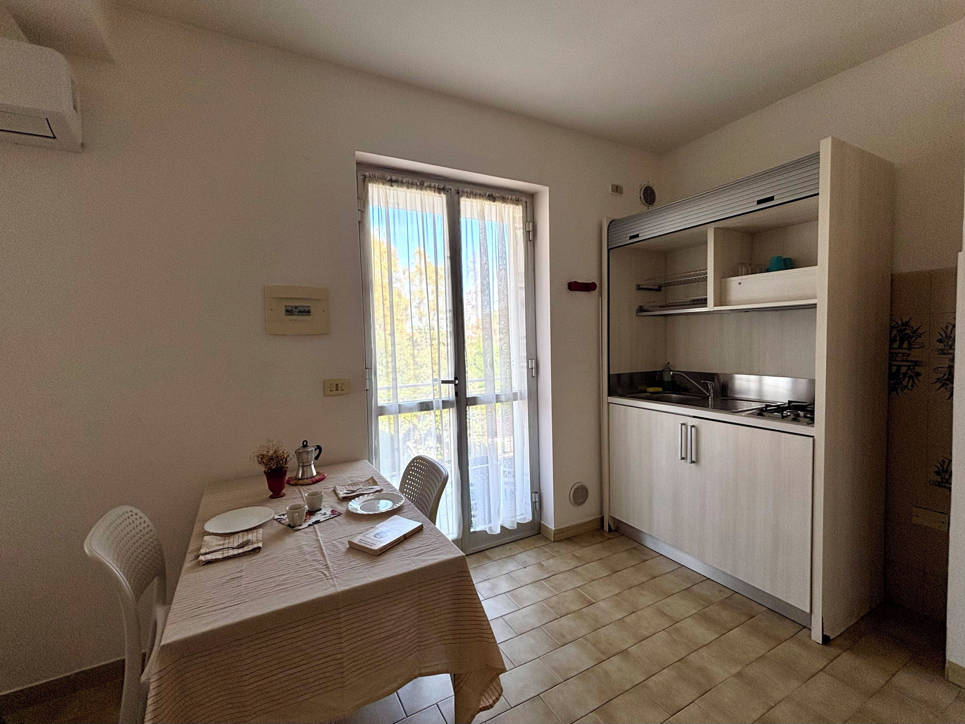 A compact kitchen with a dining area, a window with curtains, and a tiled floor.